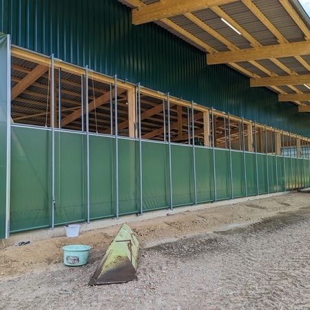 Unter blauen Himmel ist ein grüner Stall von außen mit Agrotel Seitenlüftungssystem 4 zusehen