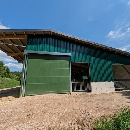 Ein grüner Stall der durch ein Agrotel Rolltor betreten werden kann