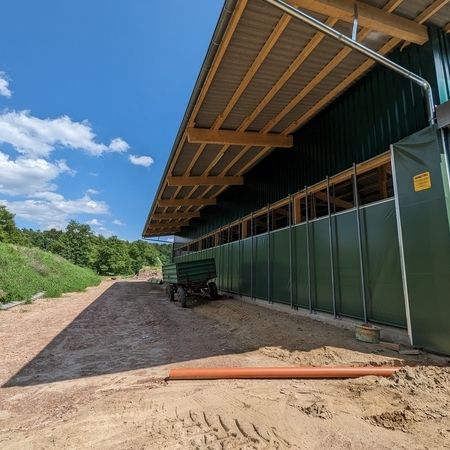 Unter blauen Himmel ist ein grüner Stall von außen mit Agrotel Seitenlüftungssystem 4 zusehen